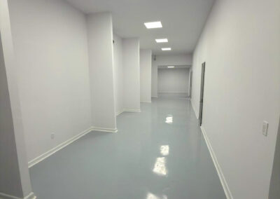 Pasillo industrial con paredes blancas, piso epóxico gris y zoclo sanitario de PVC para inocuidad alimentaria